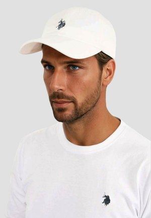 White baseball cap with embroidered black polo player logo. Worn with a white crew-neck t-shirt featuring a small matching logo.