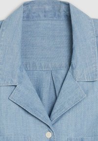 Light blue chambray shirt featuring a notched collar, a single button closure, and a subtle texture with minimal stitching details.