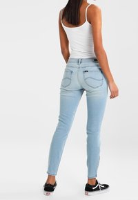 Ljust blå smala jeans med en slät yta, bakfickor och midjehöjd, kombinerat med svarta skor och en vit linne.