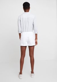 Vita bomullsshorts med rak skärning, kombinerade med en ljusgrå randig långärmad skjorta, bar tillsammans med vita sneakers.