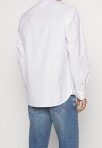 Camicia bianca a maniche lunghe con orlo curvo e polsini abbottonati, realizzata in tessuto di cotone, abbinata a jeans in denim di lavaggio medio.