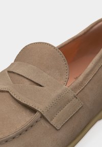 Μπεζ μοκασίνι από σουέντ με λεπτομέρεια κοψίματος στο λουράκι στην κορυφή και διακοσμητικό ράψιμο κατά μήκος των άκρων.