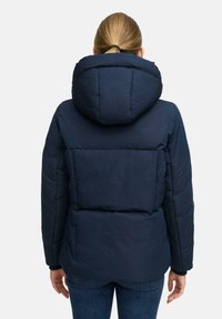 Marineblauwe gewatteerde jas met een grote, gewatteerde capuchon, gestreepte textuur en een slanke pasvorm. Bevat een opvallend achterpaneel en handopeningen bij de mouwen.