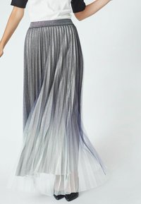 Fustă maxi plisată metalică, cu un gradient de la argintiu la alb transparent în partea de jos, dotată cu un talie confortabilă și un ușor luciu.