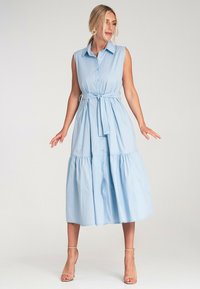 Jasnoniebieska, bezrękawnikowa sukienka z guzikami z przodu, kołnierzykiem i paskiem w talii. Posiada warstwową spódnicę, która sięga poniżej łydki. Gładka tekstura.