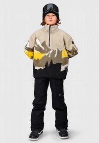 Pullover in pile con motivo montagna nei toni del beige, grigio e giallo. Abbinato a pantaloni neri e sneaker nere, con collo alto e zip.