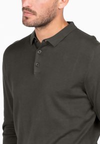 Polo a maniche lunghe verde scuro realizzato in cotone a coste, con colletto e chiusura a tre bottoni.