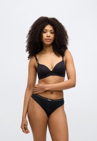 Čierna podprsenka s hladkou tkaninou, hlbokým výstrihom a nastaviteľnými ramienkami. Zodpovedajúce čierne nohavičky s pásom s logom. Jednoduchý, klasický dizajn.