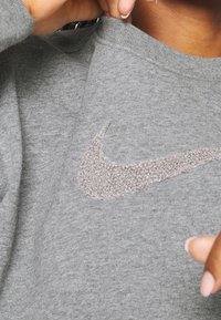 Szara bluza z teksturowanym, jasnoszarym logo Nike z przodu, z prążkowanym dekoltem i miękką fakturą materiału.