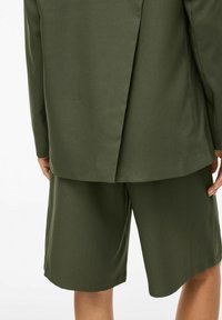 Blazer ajusté vert foncé avec une fente et un short assorti jusqu'aux genoux, présentant une texture lisse et sans motifs visibles.