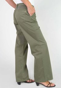 Olijfgroene katoenen broek met wijde pijpen, zijzakken, een achterzak en een subtiele logo-accent op de tailleband. Zachte textuur.