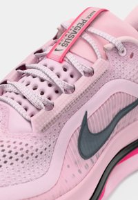 Gros plan sur une chaussure de running Nike Pegasus Premium rose avec des lacets à motif, une tige en mesh et le logo Swoosh noir de Nike sur le côté.
