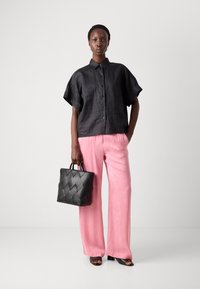 Camicia nera con bottoni e maniche corte; pantaloni larghi alla caviglia di un leggero colore rosa chiaro; borsa nera testurizzata con motivo intrecciato; sandali neri aperti.