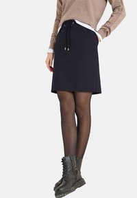 Marineblauer Rock mit Kordelzug und geradem Schnitt, aus weichem Stoff. Kombiniert mit einem braunen Pullover und schwarzen Schnürstiefeln.