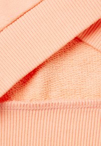 Tissu en tricot en corail doux présentant une texture côtelée aux poignets et une finition lisse en dessous, mettant en avant un aspect superposé et confortable.