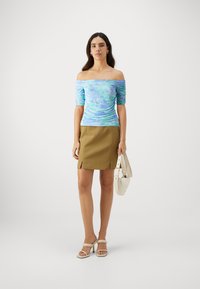 Světle modrý top bez ramínek s květinovým vzorem a řasenou texturou, doplněný khaki mini sukní. Modelka drží bílou kabelku a má na sobě béžové lodičky.