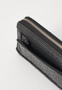 Portafoglio nero con chiusura a zip, superficie testurizzata e motivo logo. Presenta più scomparti e un accento con zip dorata.