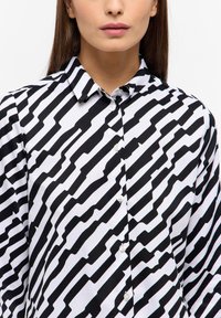 Black and white patterned button-up shirt with a collar; features wavy lines and solid stripes; made of smooth fabric with a fitted design.