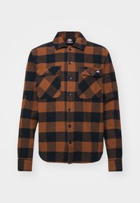 Camisa de franela a cuadros marrón y negra, de mangas largas, con dos bolsillos delanteros con solapas, cierre de botones, textura suave y cuello estándar.