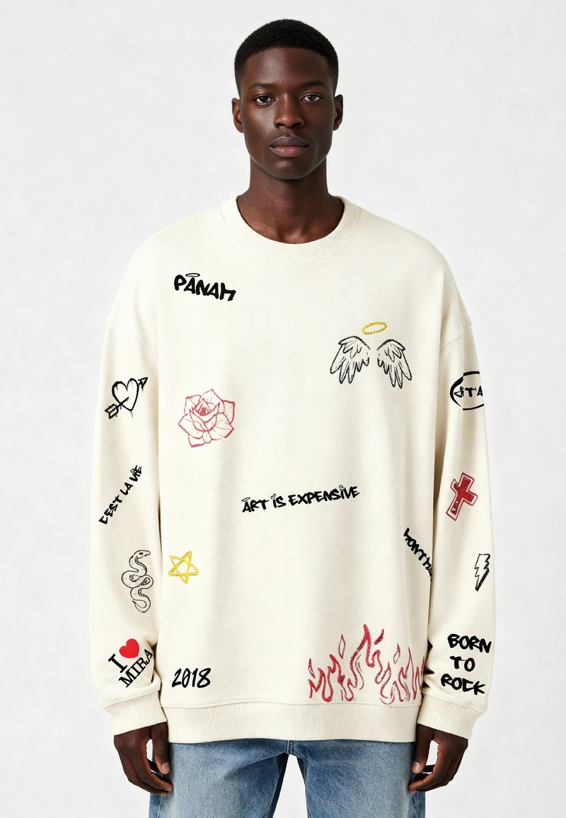 Sudadera color crema con diversos diseños bordados coloridos, que incluyen una rosa, alas de ángel y frases de texto, con puños acanalados.