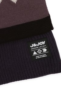 Gebreide beanie in gradiënttinten van paars en zwart, voorzien van een zwart label met witte graphics en tekst over Andes-erfgoed.