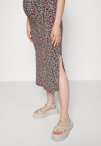 Vestido midi com estampa floral e fendas laterais, apresentando fundo preto e pequenas flores coloridas. Combinado com sandálias de plataforma verde-claro.