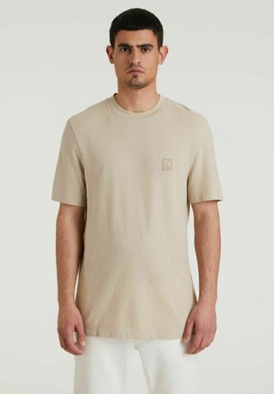 Beige katoenen T-shirt met een ronde hals, korte mouwen en een klein vierkant logo in de bovenlinkerhoek. Soepele textuur.