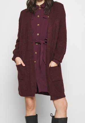 Burgundy neulejakku avoimella edessä, pitkät hihat ja sivutaskut, päällä napillinen mekko samassa värissä.