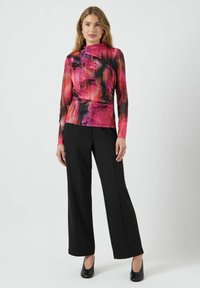 Top met lange mouwen in een levendig roze en zwart bloemenpatroon, nauwsluitend model, gecombineerd met zwarte high-waisted broek en zwarte hakken.