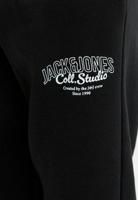 Crni dukserica s bijelim izvezenim logotipom na rukavu koji glasi "JACK&JONES Coll. Studio" i uključuje drugi tekst manjim fontom.