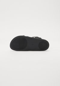 Black sandal sole with a textured rubber surface, curved shape, and two arch supports for comfort. Flat design suitable for casual wear.