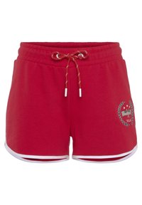 Red cotton shorts with an elastic waistband, white drawstring, side slits, and a logo with laurel accents on one leg.