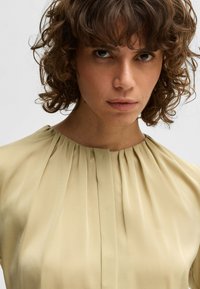 Licht olijfgroene blouse met een geplooide halslijn en zachte, gladde stof. Het ontwerp heeft een ronde kraag en een ontspannen pasvorm.