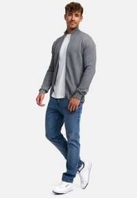 Grå hettejakke med et strukturert chevronmønster, sammen med en hvit t-skjorte og blå jeans; brukt med hvite joggesko.