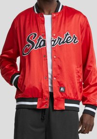 Rød satin bomberjakke med sorte og hvide stribede manchetter, med "Starter" i fed sort skrift på brystet og lukning med trykknapper.