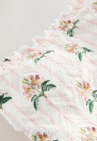 Tessuto bianco con motivi a zigzag e puntini in rilievo, decorato con stampe floreali rosa e gialle e foglie verdi, rifinito con un bordo arricciato.