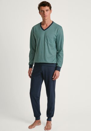 Green patterned long-sleeve top with V-neck and chest pocket, paired with dark blue tapered pants, both made of soft fabric.
