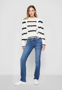Gilet en tricot rayé blanc et marine avec des boutons, associé à un jean bleu et des baskets blanches. Présente un design court et un tricot texturé.