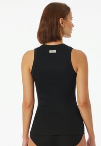 Zwarte geribbelde tanktop heeft een getailleerd ontwerp met een ronde halslijn en een label op de achterkant. De stof is glad en rekbaar.