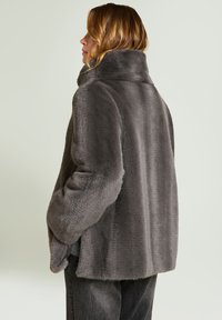 Grijze jas van nepbont met een hoge kraag, lagere schouders en een losse pasvorm. Zachte textuur met een gladde afwerking en zijzakken.