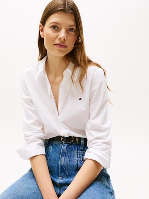 Witte button-up shirt met opgerolde mouwen, gedragen in een hoge taille blauwe denim jeans, met een zwarte riem met een gouden ronde gesp.