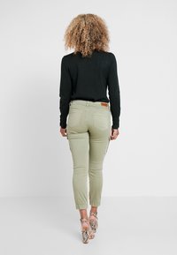 Ljust gröna cargobyxor med elastiska muddarna, två sidofickor och en brun logopatch på den bakre midjebandet, kombinerat med en svart topp och mönstrade klackar.