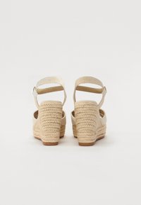 Beige kilehæler sandaler med en vævet reb hæl, der har en tekstureret stof ankelrem og åben bagdesign.