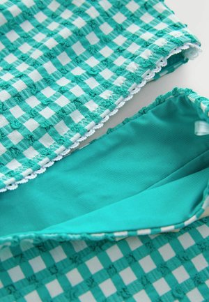 Makro záber tyrkysovo-bielenej kárované textúrovanej látky s drobnými prešívanými detailmi a tyrkysovo-zelenej vnútornej podšívky so zvraštenými okrajmi.