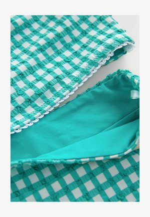 Detaljan prikaz tirkizno-bijele tkanine s kariranim teksturom, malim ušivenim detaljima i tirkiznom unutarnjom podstavom s naboranim rubovima.