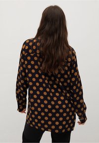Pitkähihaisen mustan paidan, jossa on suuria ruskeita pilkkuja, rento istuvuus, nappi hihansuut ja klassinen kaulus. Suloinen kangas.