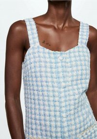 Texturovaný modro-bílý kostkovaný top s širokými ramínky, hranatým výstřihem a předními knoflíky. Materiál vypadá tkaný a lehký.
