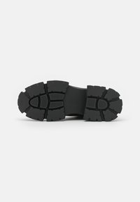 Semelle de chaussure en caoutchouc noir présentant un motif de profondeur pour une meilleure traction, avec des sections texturées et une forme contour pour le confort.