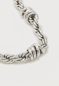 Κοντινό πλάνο ασημένιας, γυαλιστερής, στριφτής αλυσίδας με ένα λείο, σπειροειδές δαχτυλίδι διακοσμητικό σε ανοιχτό φόντο.