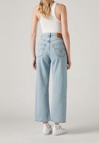 Högmidjade ljusblå denimjeans med en avslappnad, bred benpassform, utrustade med två bakfickor och en ljusbrun läderetikett vid midjan.